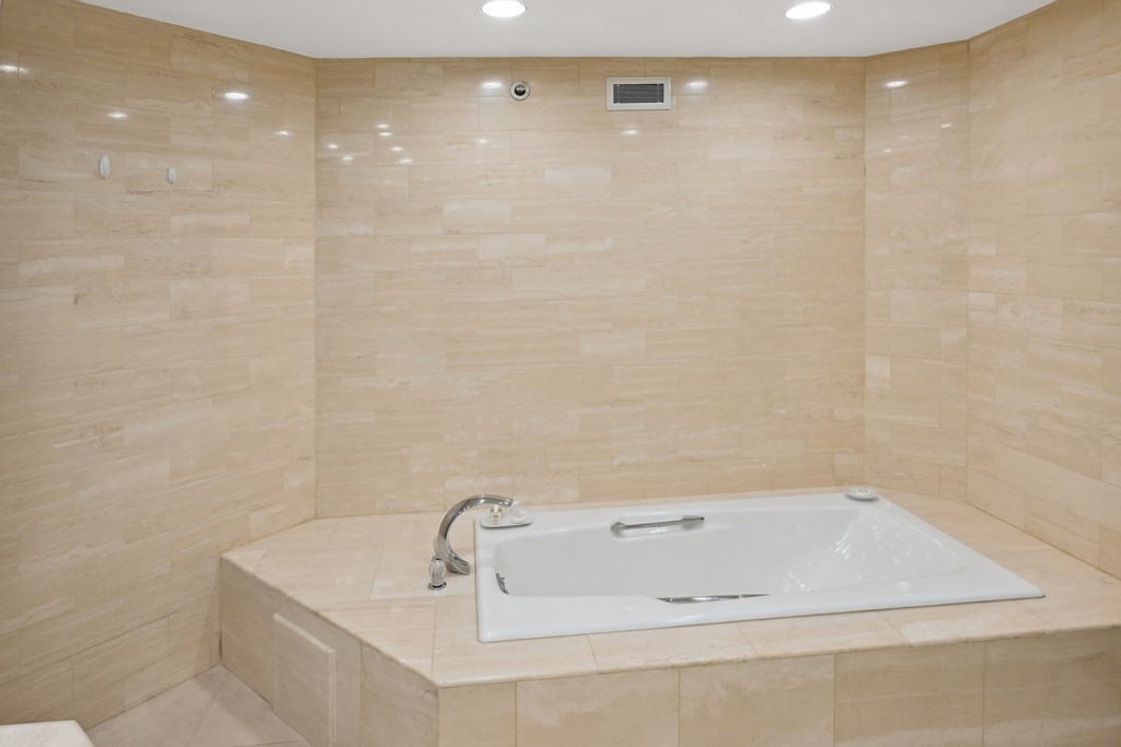 a large white bath tub in a bathroom with beige tiles