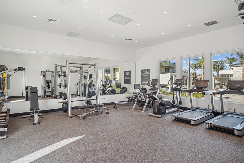 A spacious gym with a variety of equipment including treadmills, weights, and exercise machines at The Max on Jefferson Apartments, California, 92562