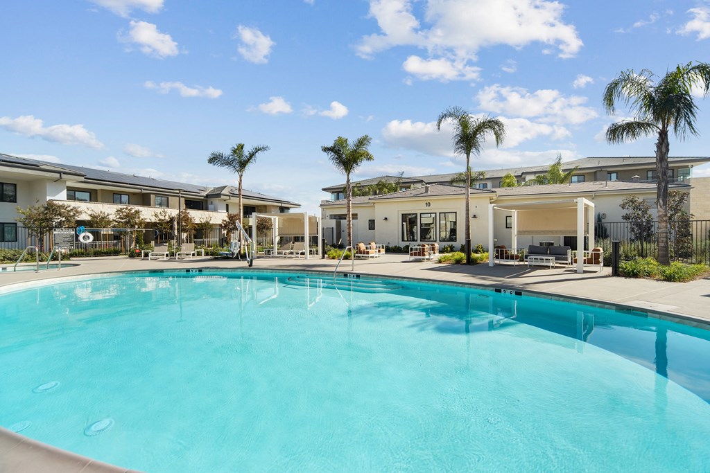 A large swimming pool in front of a building with palm trees at The Max on Jefferson Apartments, California