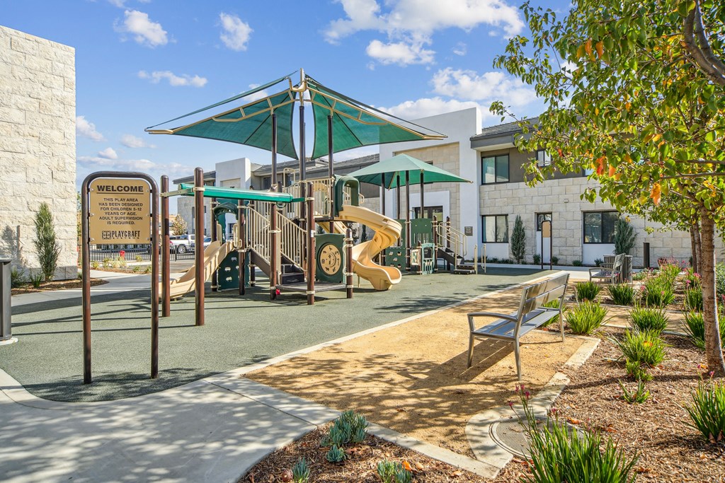 A playground with a slide, a bench and a tree at The Max on Jefferson Apartments, Murrieta, CA, 92562