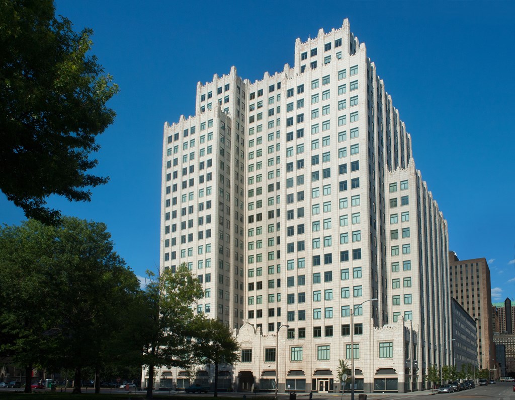 A large white building with many windows is surrounded by trees.