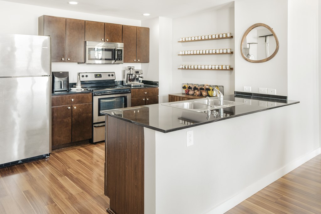 A modern kitchen with a refrigerator, microwave, oven, sink, and wooden cabinets.