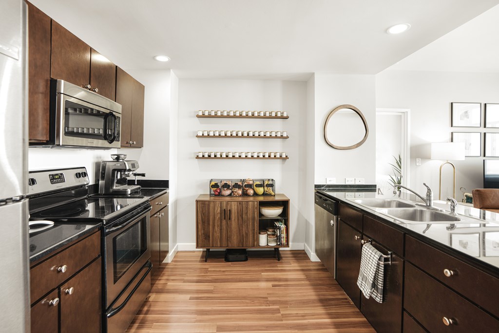 A modern kitchen with dark wood floors and stainless steel appliances.