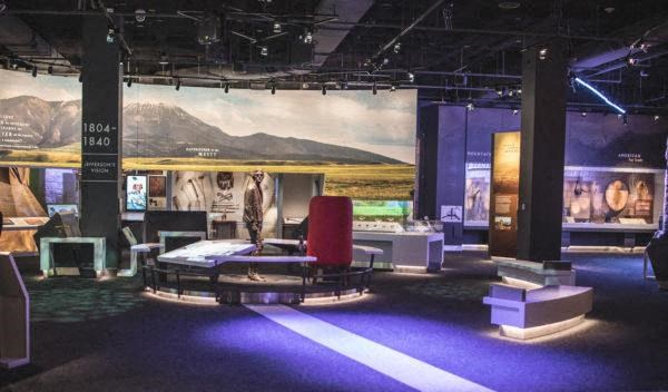 a room filled with lots of furniture and a large screen at the new Gateway Arch museum
