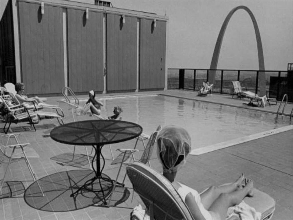 Circa 1960 photo of a woman sitting in a chair next to the rooftop swimming pool with the Gateway Arch monument in the background