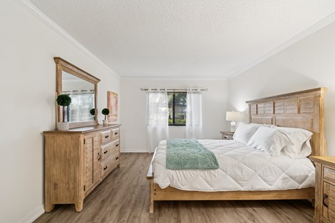 A bedroom with a large bed, a dresser, and a mirror at Hampton Apartments, Clearwater, FL, 33759