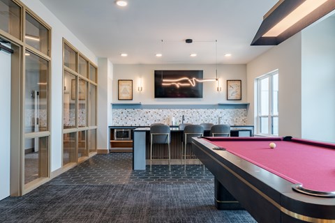 A pool table is in the middle of a room with a bar and a television.