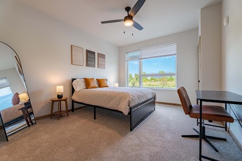A bedroom with a bed, chair, and a ceiling fan.