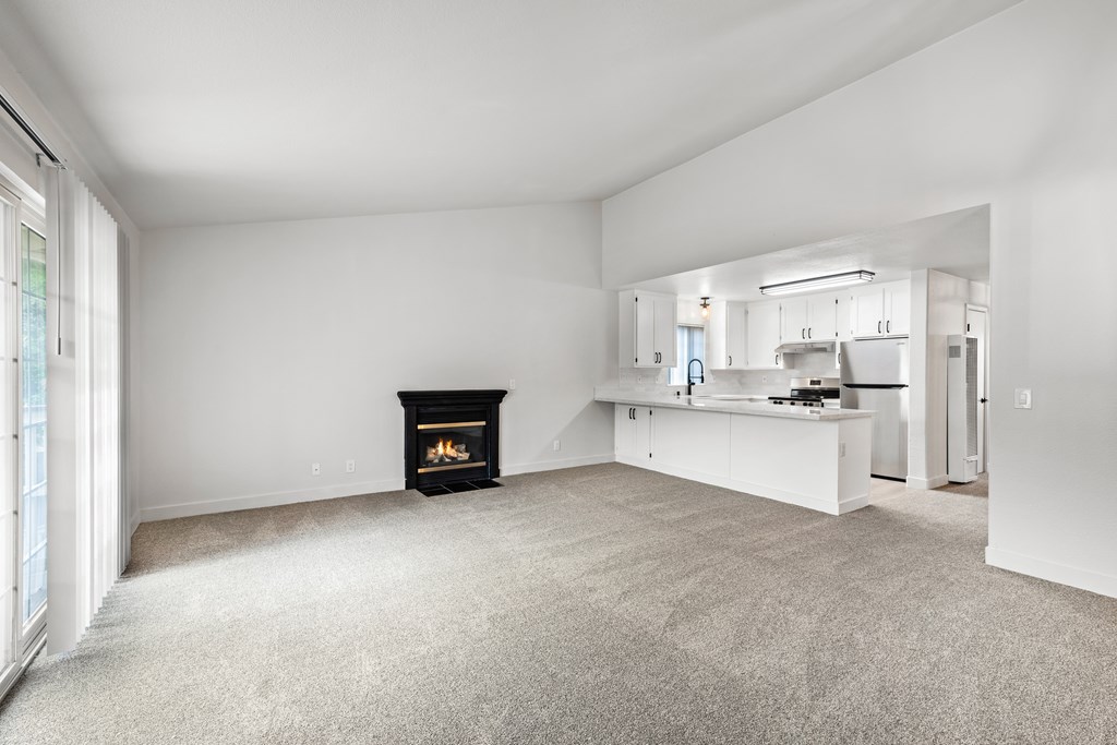 A living room with a fireplace and a kitchen in the background.