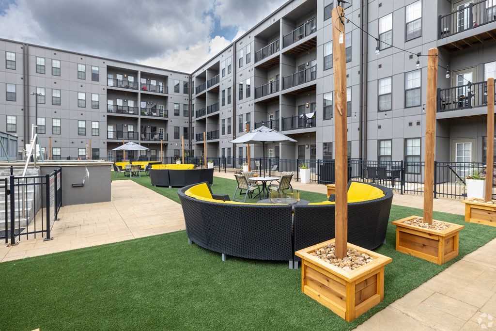 an outdoor lounge area with tables and chairs in front of an apartment building