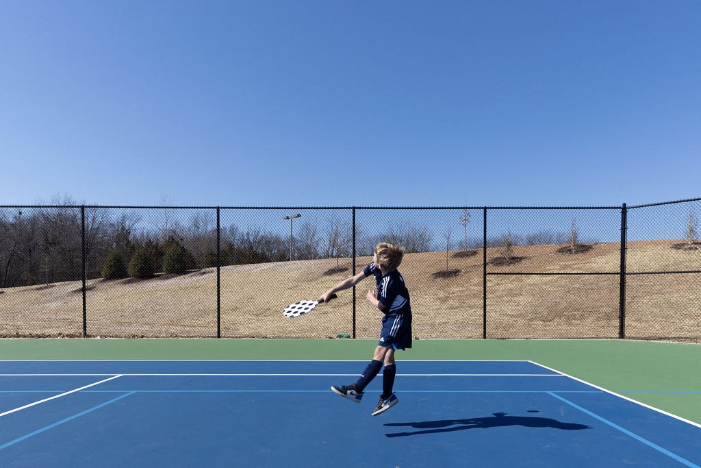 a young boy jumping in the air with a tennis racket at The Residences at Tesson Ridge, Saint Louis