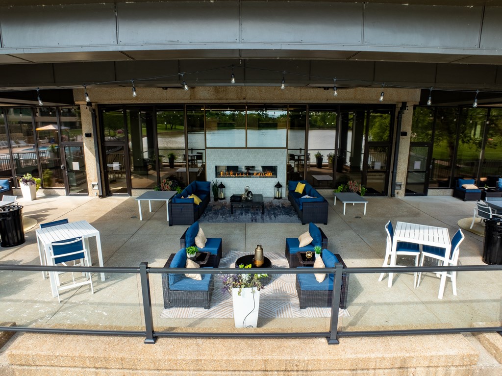 A patio with blue chairs and a table with a vase of flowers on it.