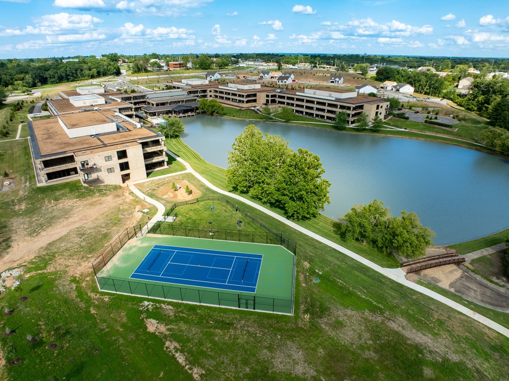 A tennis court is located on a grassy area next to a lake.
