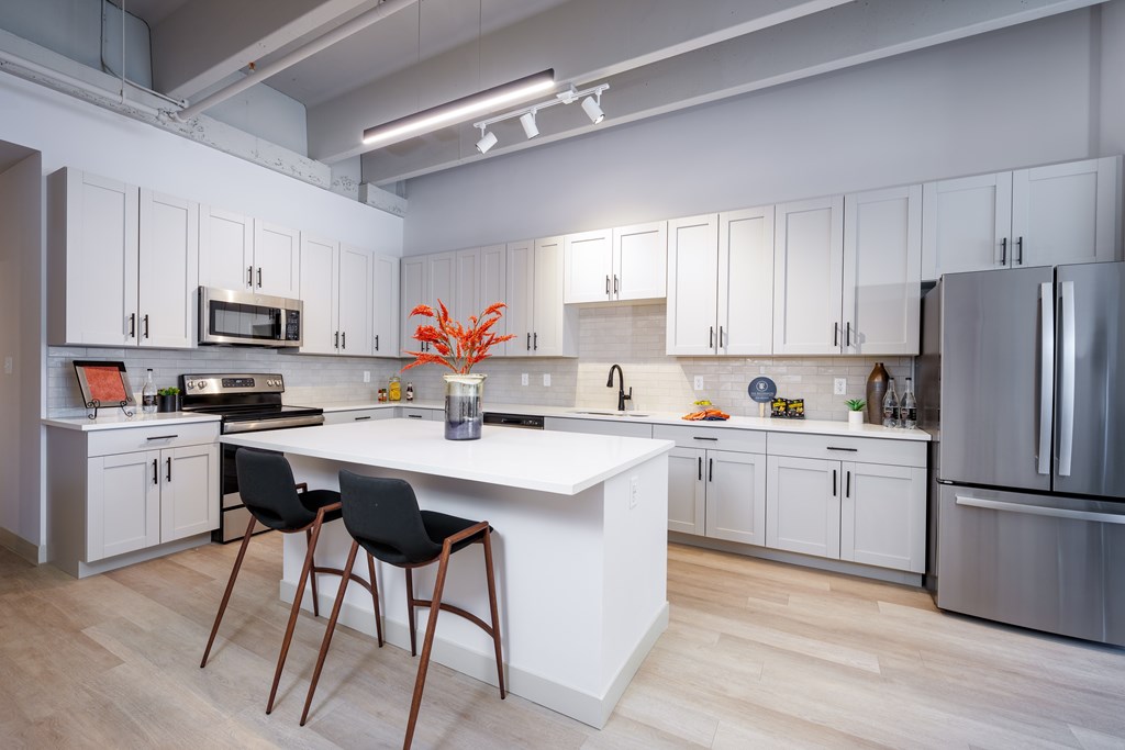 A kitchen with white cabinets and a white island with two black chairs.
