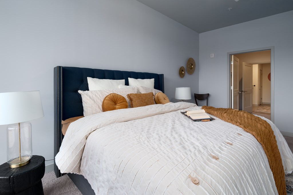 A bed with a white comforter and a blue headboard with a gold pillow and a book on it.