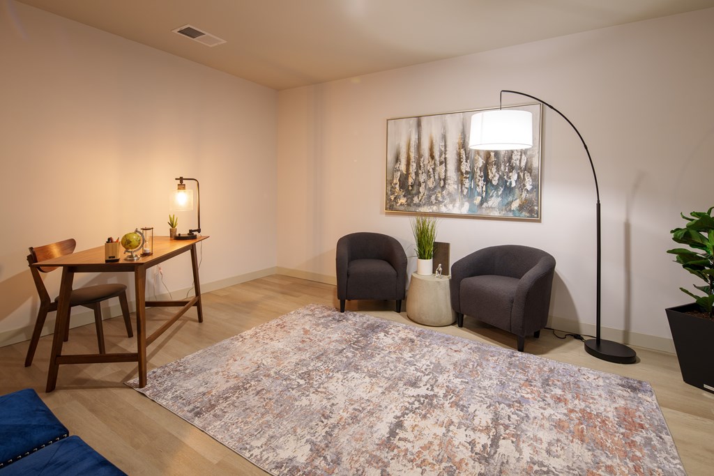 A room with a rug, a table with chairs, a floor lamp, and a painting on the wall.
