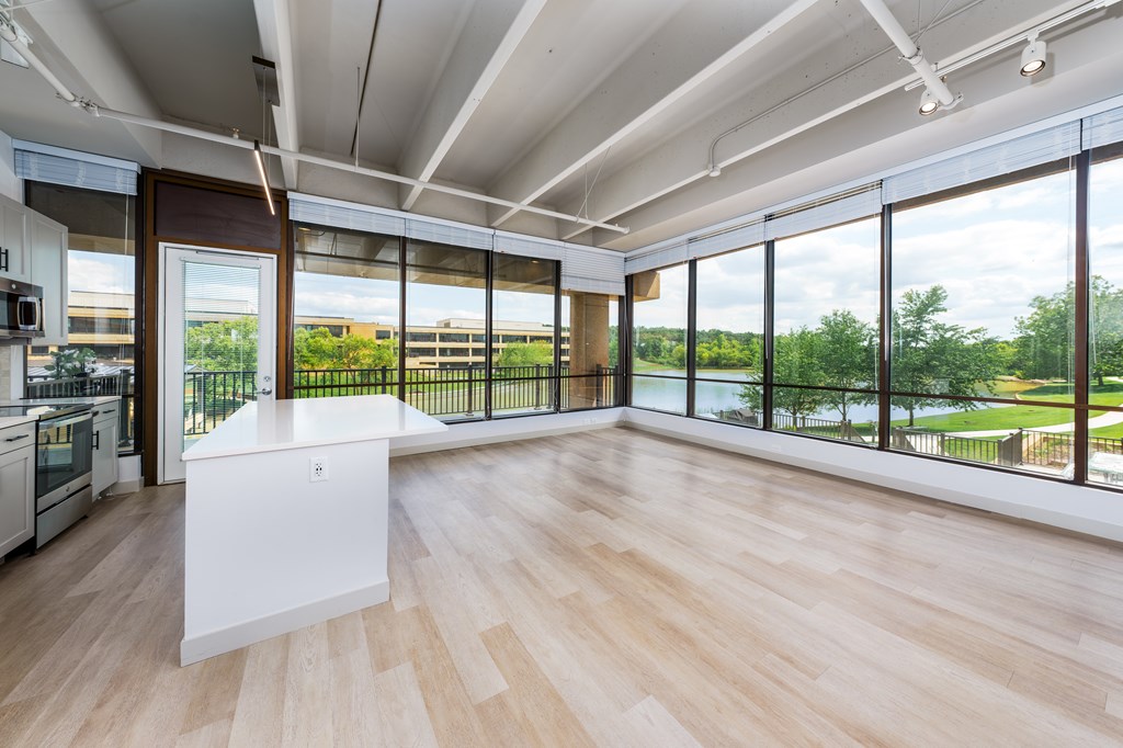 A kitchen with a white island in the middle of a room with wooden floors and a large window.