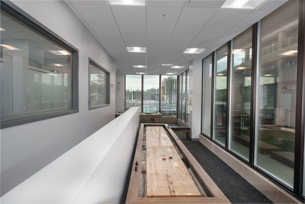 A long wooden table with a red object on it sits in a room with white walls and windows.