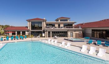 A large swimming pool with lounge chairs in front of a multi-story building.