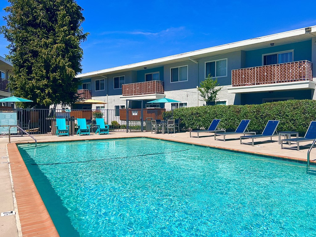a swimming pool with blue chairs and a building in the background