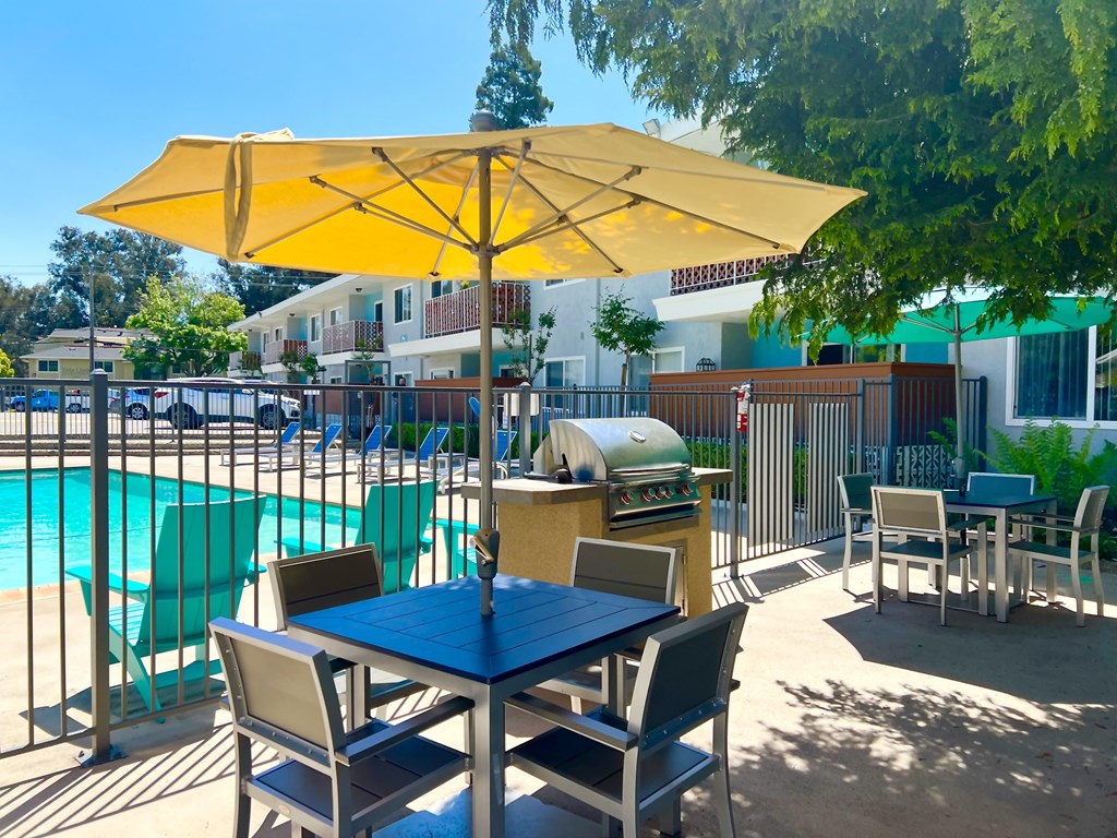 a patio with a table and chairs with an umbrella and a swimming pool