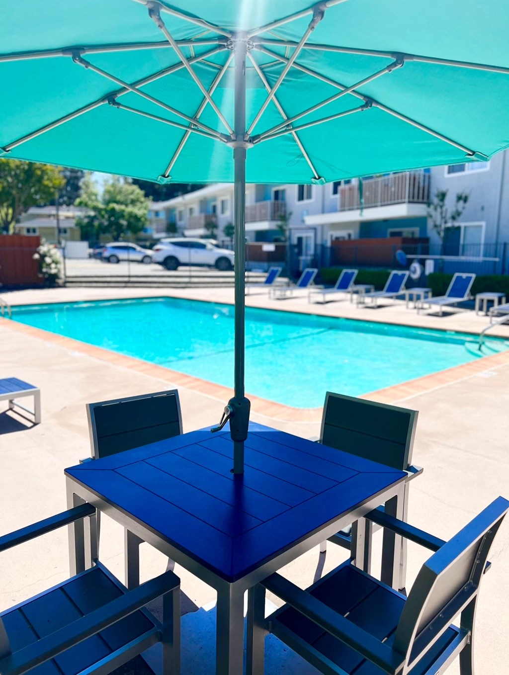 a dining table with an umbrella next to a swimming pool