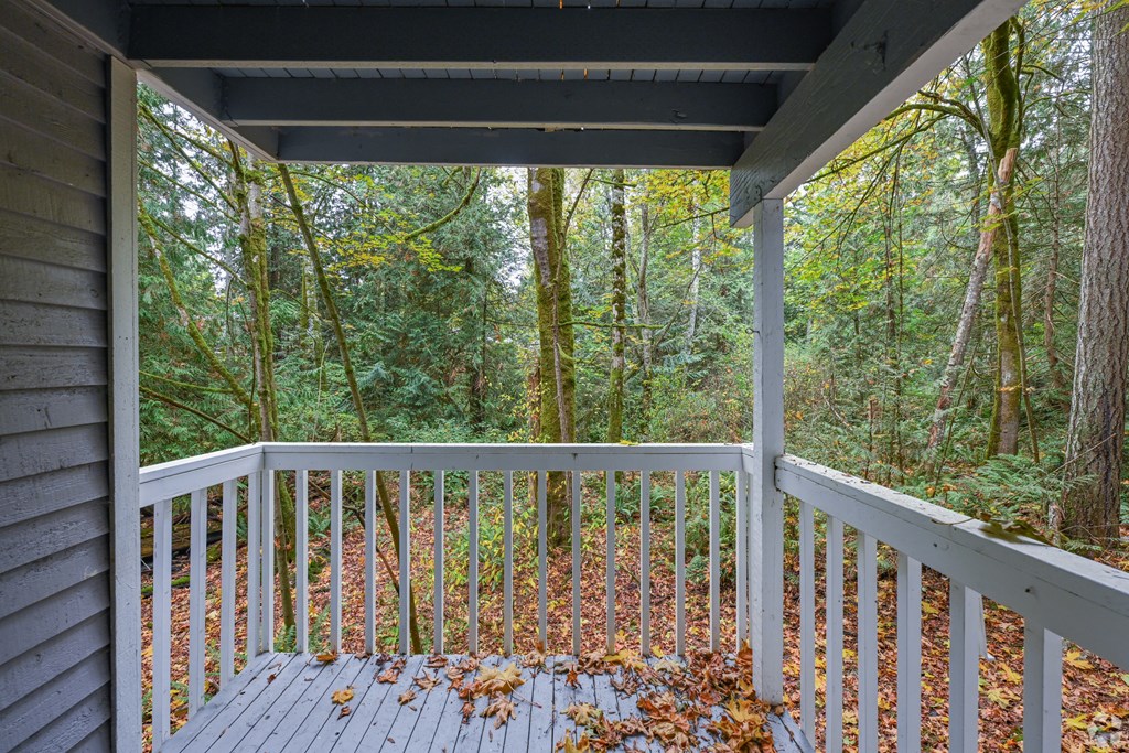 A wooden deck with a railing and leaves on the ground.