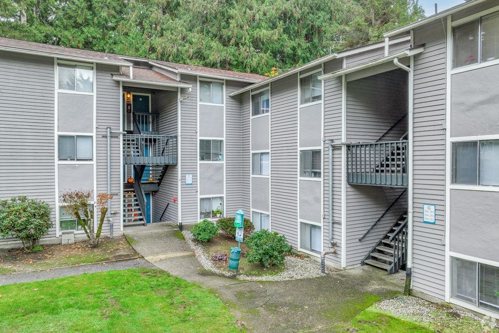 A grey apartment building with a small garden in front.