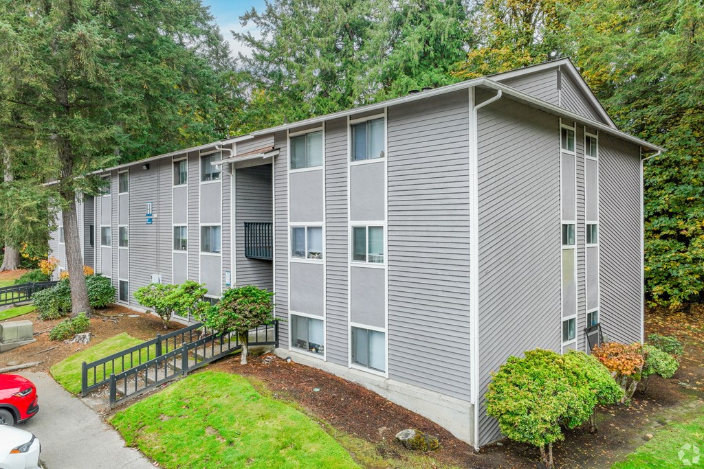 A grey apartment building with a red car parked in front.