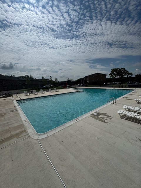 A large outdoor swimming pool with sun loungers and a cloudy sky.