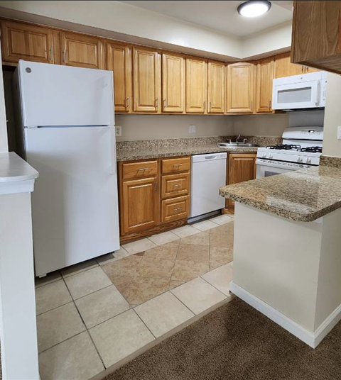 A kitchen with a white refrigerator, brown cabinets, and a granite countertop.