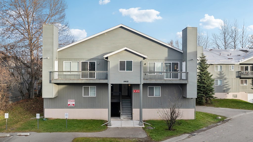 A grey two-story apartment building with a balcony on the second floor.