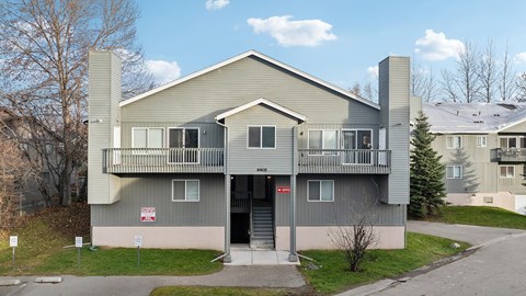 A grey two-story apartment building with a balcony on the second floor.