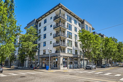 A street view of a white building with balconies and trees in front.
