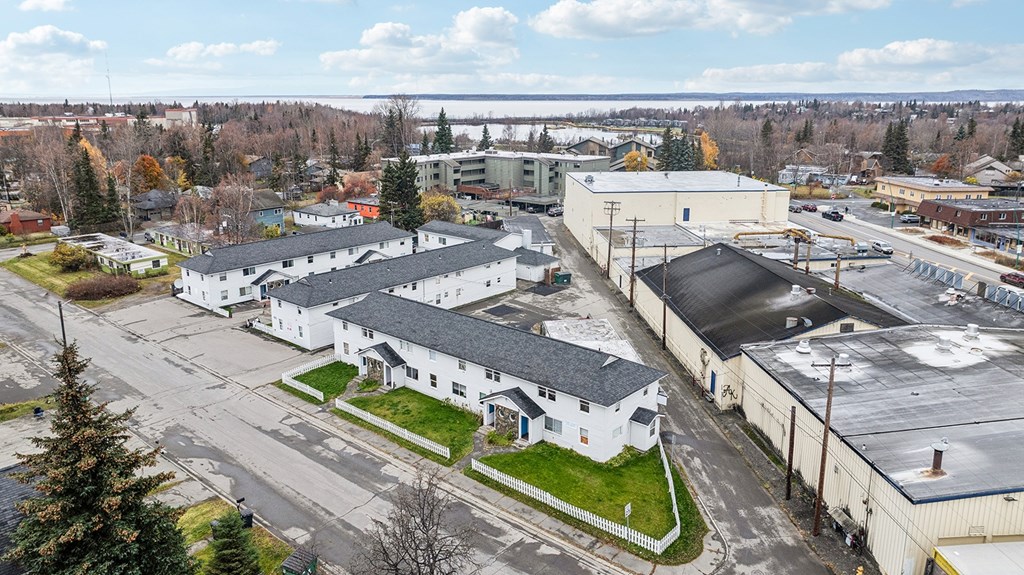 A large white building with a black roof is surrounded by other buildings and trees.