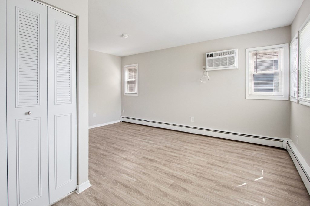 A room with a white door, a window with blinds, and a wall-mounted air conditioner unit.