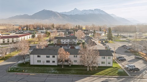 A large white building sits in the middle of a parking lot with mountains in the background.