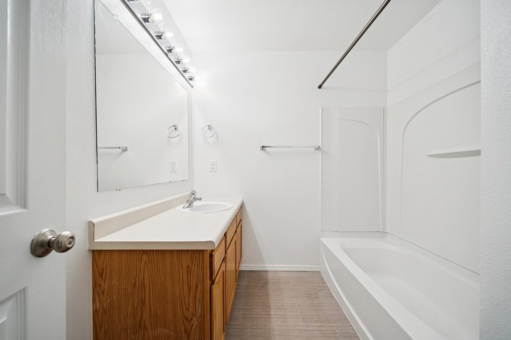 A white bathroom with a sink, mirror, and bathtub.
