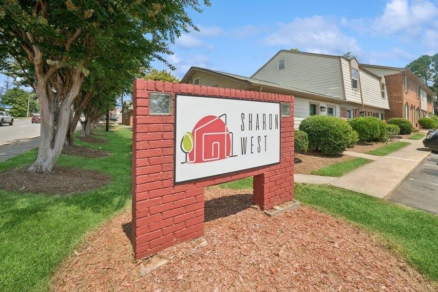 A sign for Sharon West in front of a tree and houses.