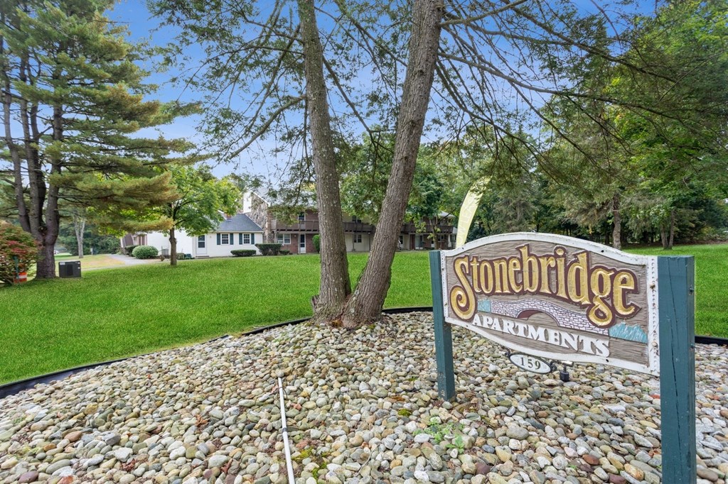 a sign for stonebridge apartments in front of a lawn and trees at Stonebridge, Ellington, CT