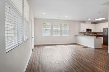 an empty living room with a kitchen in the background