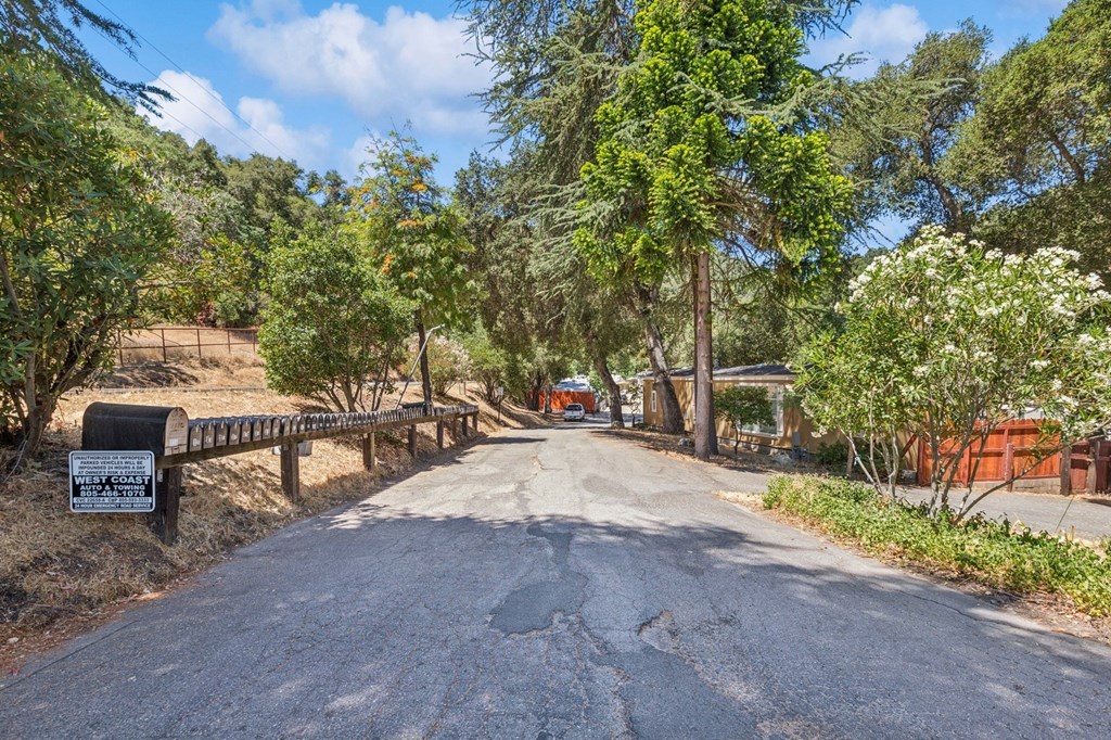A gravel road leads to a sign on the left and a fence on the right.