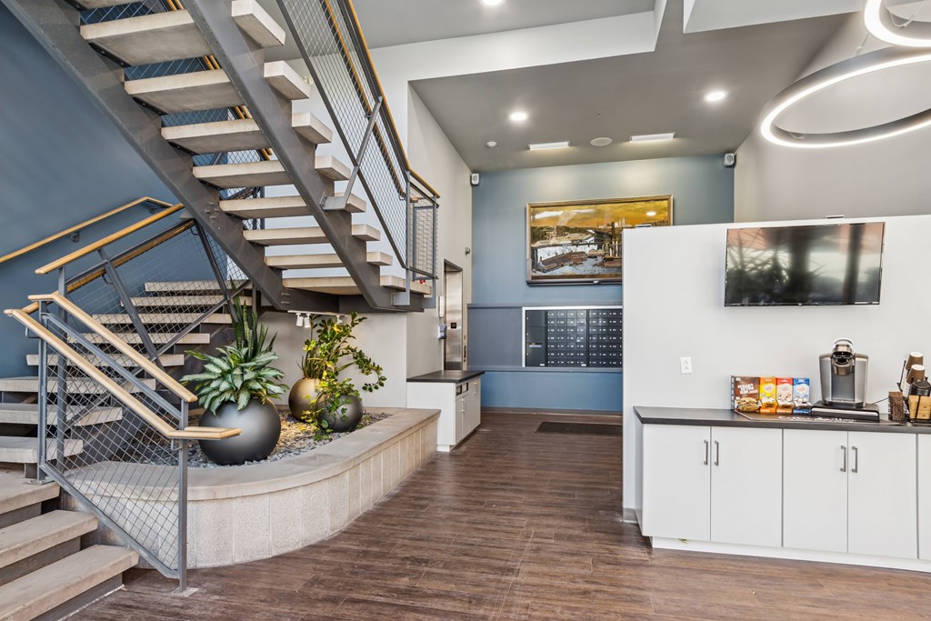 A staircase with a metal railing and wooden steps leads to a brightly lit room with a kitchen area.