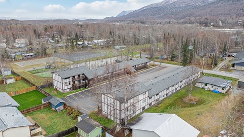 A large building with a metal roof is surrounded by smaller buildings and trees.