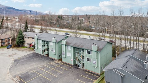 A parking lot in front of a green building with a mountain in the background.