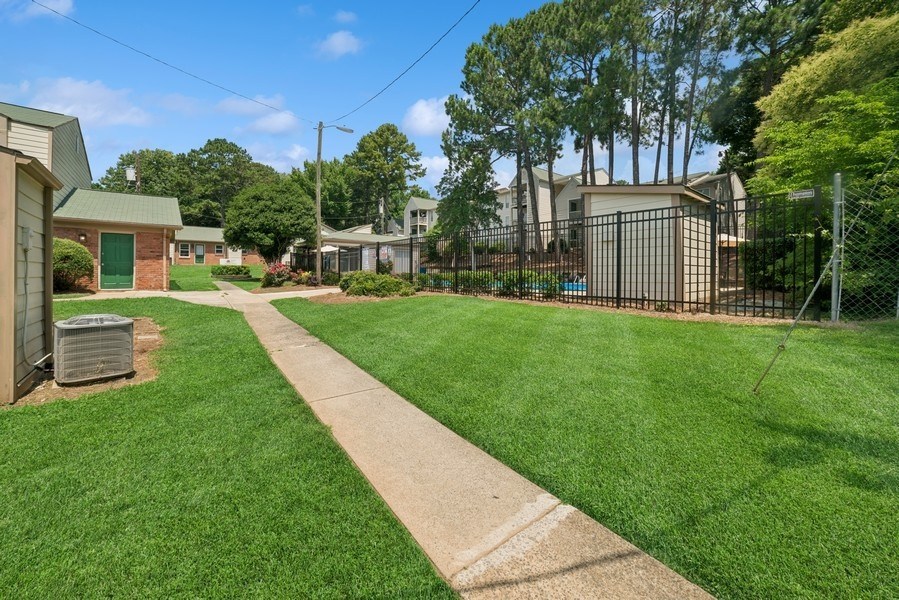 A grassy area with a concrete walkway in the foreground and a fence.