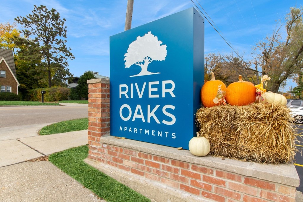 the sign for river oaks apartments in front of a brick wall with pumpkins at River Oaks, North Aurora, 60542