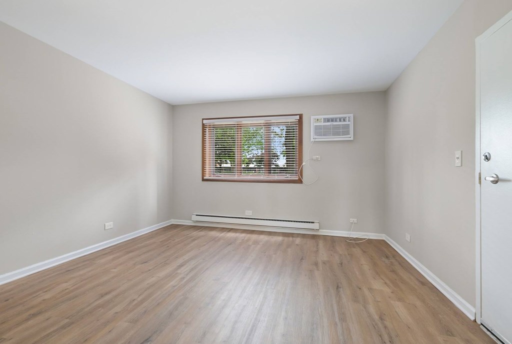 A room with wooden flooring and a window with blinds.