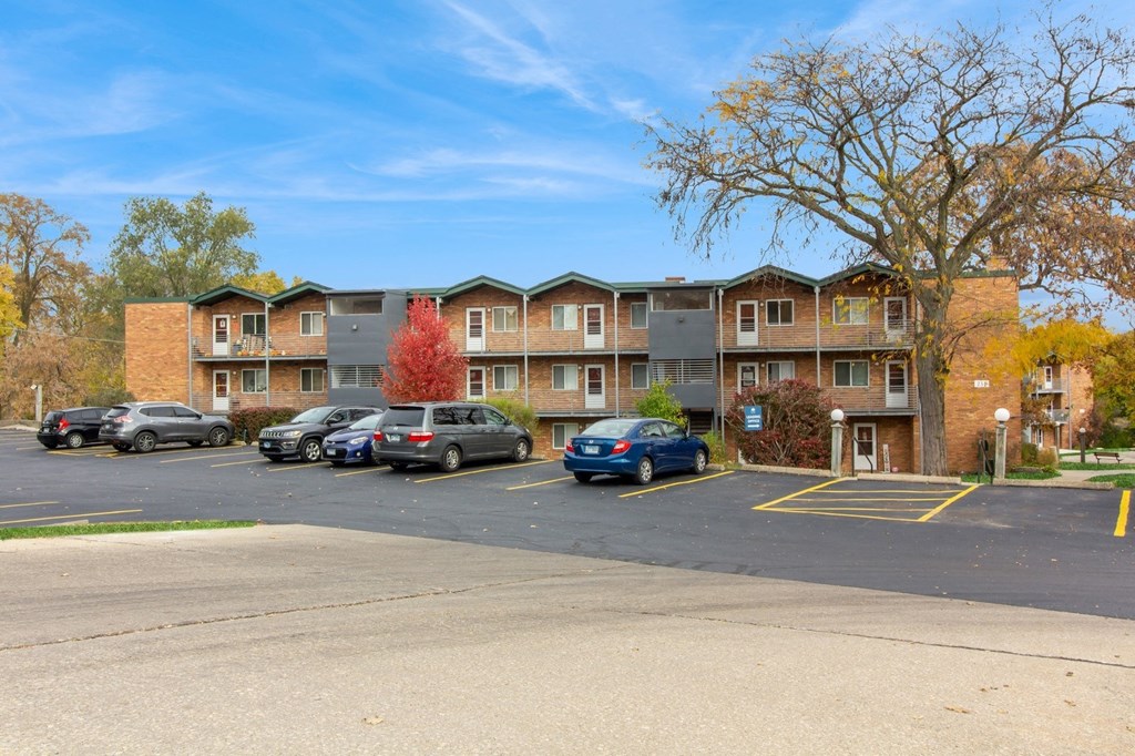an apartment complex with cars parked in a parking lot at River Oaks, North Aurora, 60542