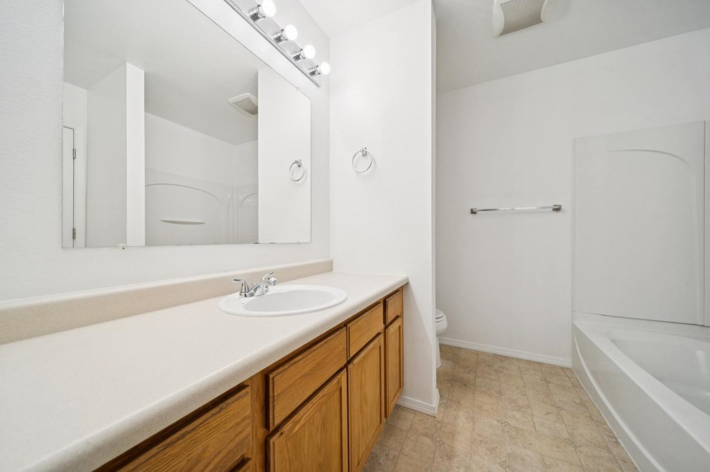 A white bathroom with a sink, mirror, and bathtub.